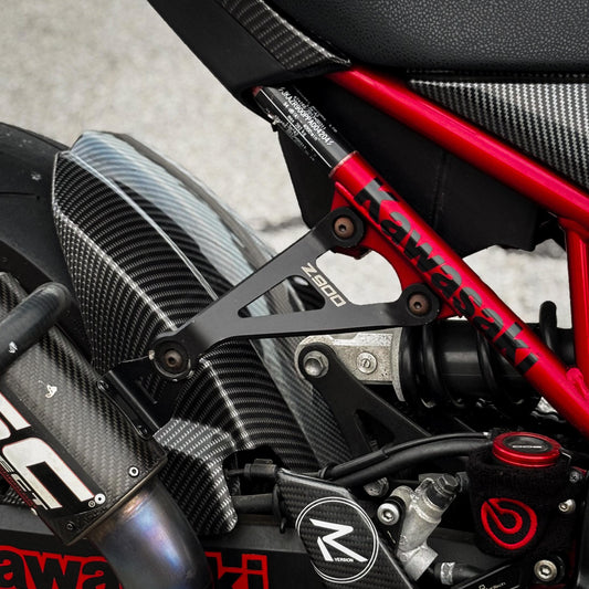Soporte de escape racing de aluminio CNC montado junto al escape de carbono de una Kawasaki Z900
