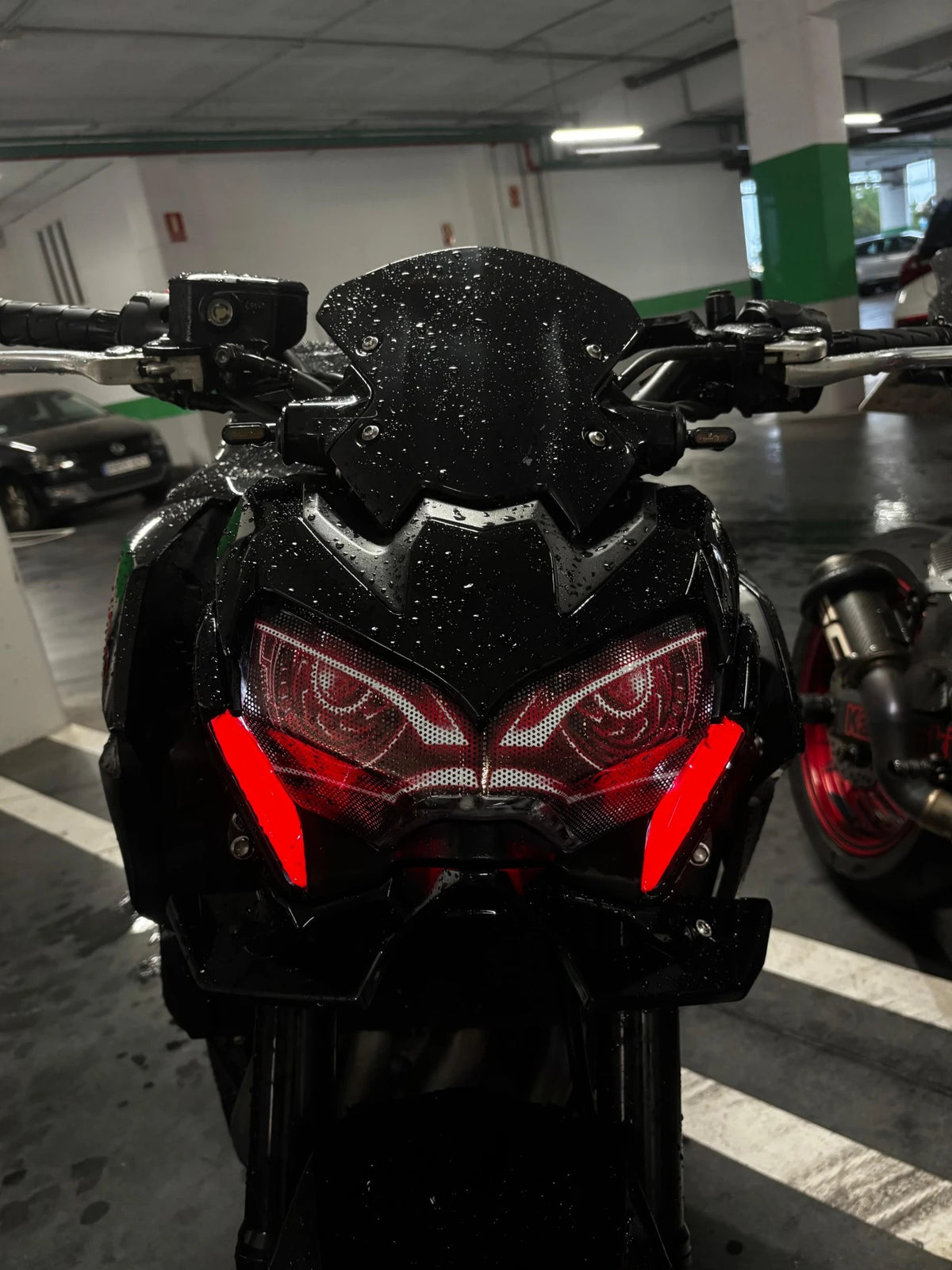 Front of the Kawasaki Z900 wet from the rain, with red eye decals and the lights on